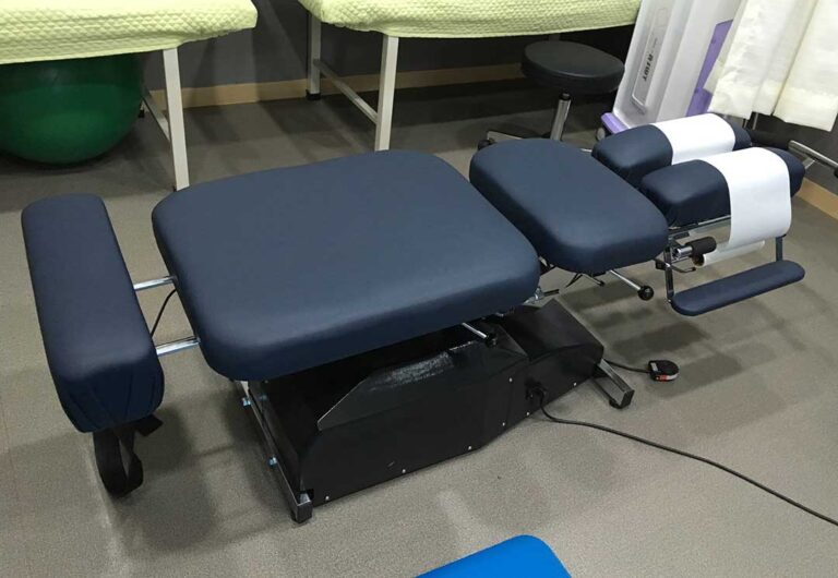 A person at home holds an ice pack to their lower back, sitting on a living room couch.